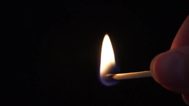 Une main allume une allumette sur une boîte, elle brûle et une main l'éteint d'un mouvement rapide. Vue latérale, fond noir.