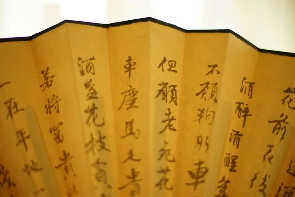 Part of an open yellow fan with brown chinese characters on it, white background, closeup