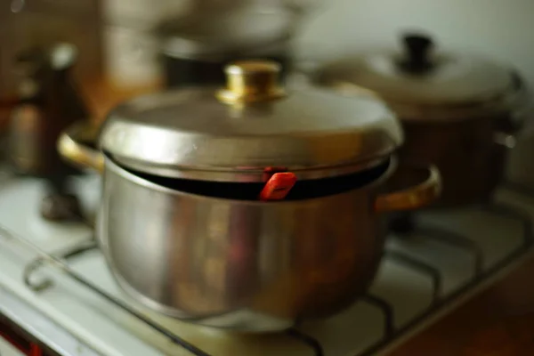 stainless steel pan with red soup ladle under the lid on the stove.