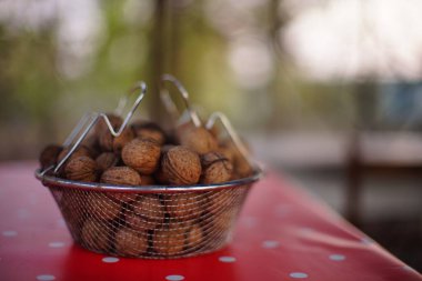 Kırmızı masa örtüsünde beyaz noktalı ceviz dolu bir ağ kasesi..