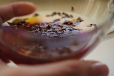 Kadın parmaklarında siyah çay olan şeffaf bir fincan.