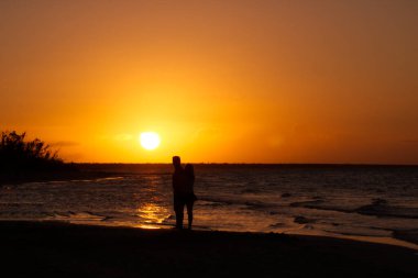 Gün batımında sahilde yürüyen bir çiftin silueti.