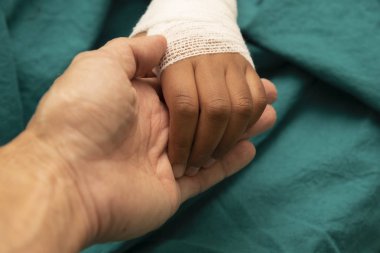 Doktor hastanede destek için gazlı bezle sarılmış bir çocuk elini tutarak