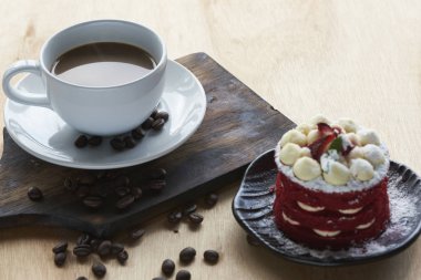 Sıcak kahve beyaz Kupası ve kahve çekirdekleri ahşap masa üzerinde. Lezzetli pasta üstüne çilek ile.