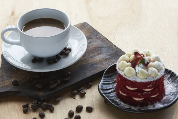 Sıcak kahve beyaz Kupası ve kahve çekirdekleri ahşap masa üzerinde. Lezzetli pasta üstüne çilek ile.