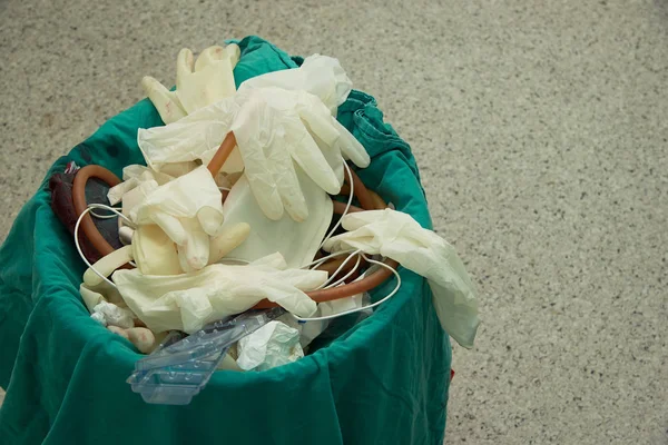 Used surgical gloves, gauzes with blood-stained, suction tube, plastic bag in garbage bin for biohazard disposal
