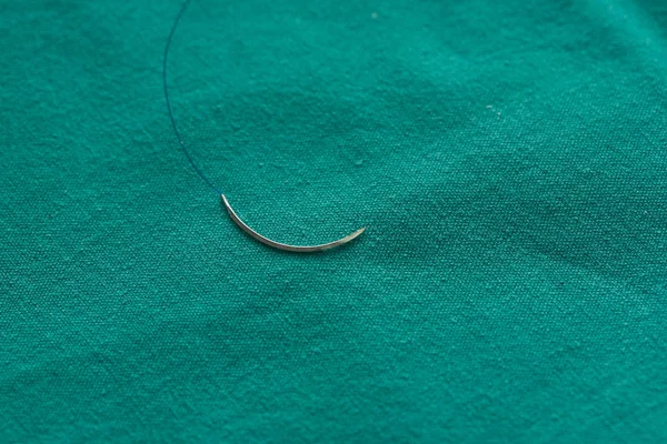 A used surgical suture with needle on the green table