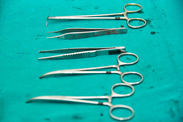 Surgical instruments includings needle holders and suture, forceps, clamps on dirty green table