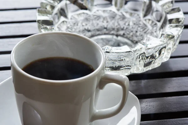 Filiżanka gorącej kawy i popielniczki na stole — Zdjęcie stockowe