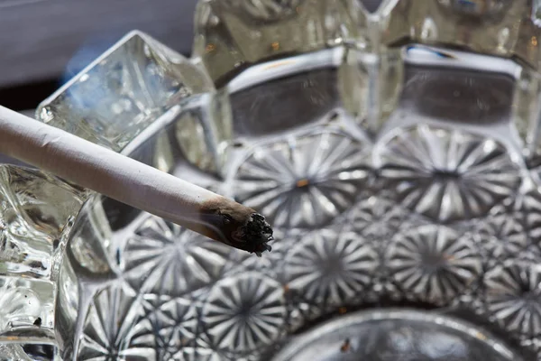 Un cigarrillo y humo en el cenicero de cristal — Foto de Stock