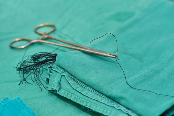 A surgical holder and needle with silk on green cloth