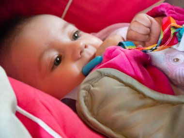 Küçük şirin beyaz bir bebek. Bebek arabasında dinleniyor, oyuncaklarını çiğniyor..