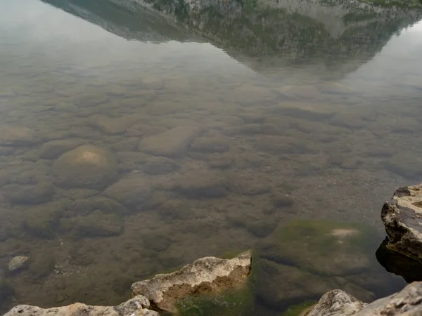 Lake with rocks in its depths. You can see reflections from the mountains around.