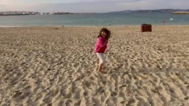 Sahilde koşan 5 yaşında bir kız çocuğu, suya doğru gidiyor. Galiçya plajı ve iklim biraz soğuk.