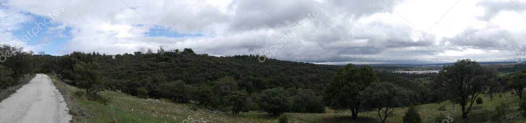 Panoramic view of the countryside, with a blue sky full of clouds, lots of vegetation and a rural road