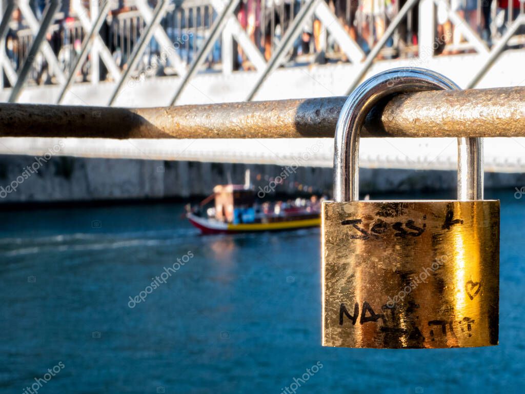 Closed lock on a banister by the Douro River, with the Dom Louis I Bridge in the background as a boat passes by
