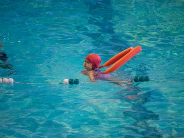 Küçük kız yüzme dersinde yüzmeyi öğreniyor.