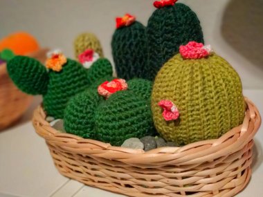 Küçük bir sepetin içinde renkli çiçeklerle süslenmiş küçük bir kaktüs ve küçük taşlar.