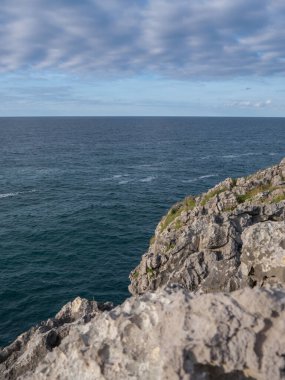 İspanya, Cantabria 'da deniz kenarındaki kayalıklarla dolu güneşli bir yaz gününde mavi gökyüzünde bir sürü bulut var.