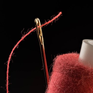 Kırmızı iplik, siyah arka planda yakın plan iğneye geçirilmiş.