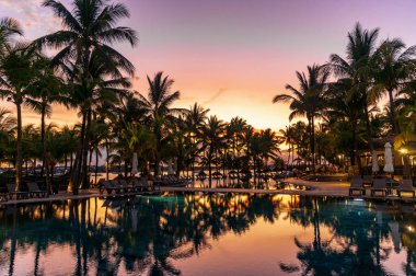 gün batımında palmiye ağaçları ve suda yansıması ile otelde yüzme havuzu