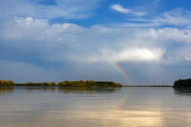 Nehirdeki manzara, mavi gökkuşağı, sonbahar ormanı olan bankanın kenarı.