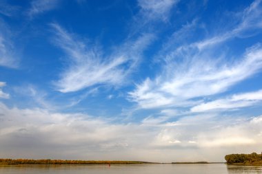 Nehirdeki manzara, bulutlu mavi gökyüzü, sonbahar ormanı kıyısı