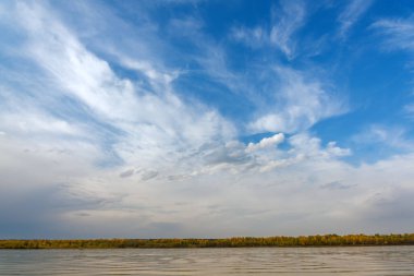 Nehirdeki manzara, bulutlu mavi gökyüzü, sonbahar ormanı kıyısı