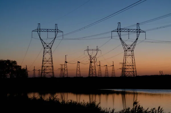 High voltage power lines in a field above a river at dawn