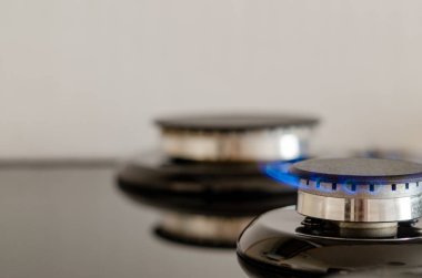 İçlerinden birinde alev olan iki gaz brülörleri. Bulanık ışık arka planda mutfak sobası. Kırpılmış yakın çekim görüntüsü