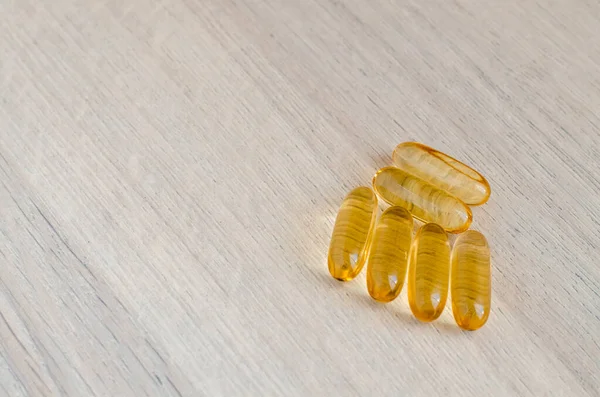 Cápsulas de laranja? com óleo de peixe em uma superfície de madeira — Fotografia de Stock