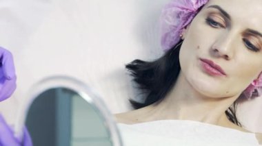 Hasta kendini dudak büyütme işlemden sonra aynaya bakıyorum ve gülümseyen bir güzellik salonu. Tıbbi kap ve ayna güzel kadın.