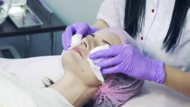 Hands in blue gloves of experienced cosmetician cleaning females face with sterile napkins. Young woman is receiving treatments in beauty salon. — Stock Video