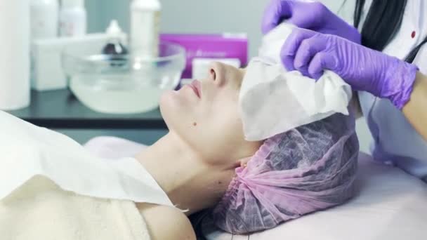 Proces van verwijdering een cosmetische crème van het gezicht van een jonge vrouw met servetten in spa salon. Handen van de schoonheidsspecialist in handschoenen reinigen van gezicht. Gezichtsbehandeling huidverzorging. — Stockvideo