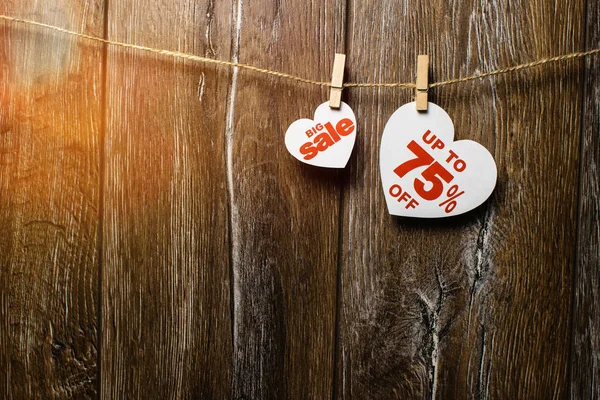 Hearts and discounts with romantic pattern on wooden background. Big sale on one heart and seventy-five percent on another hanging on rope by clothespins