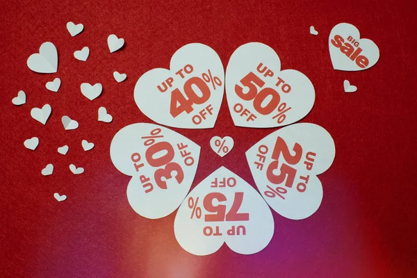 Discount promotion sale. Five big white hearts with per cent numbers surrounded by other small hearts over the red background.
