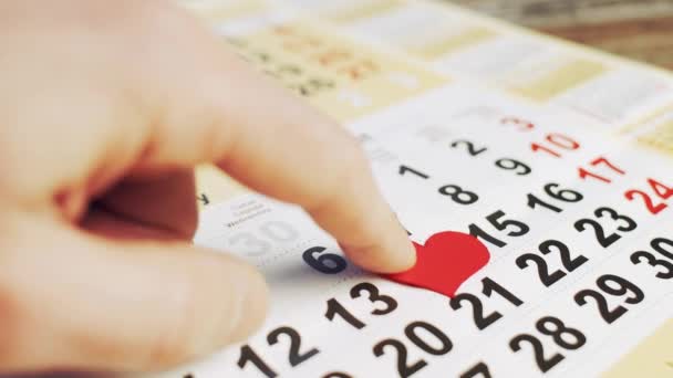 La mano mette il cuore di carta rosso al numero 14 su un calendario e un piccolo regalo con un inchino. Vacanza d'amore — Video Stock
