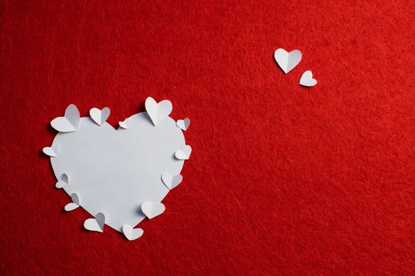 White paper heart and many small paper hearts on periphery of it over the red background. Saint Valentine\'s day