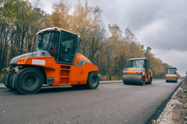 Yol Asfalt silindirleri sarı sonbahar orman arka plan üzerinde yeni bir yol döşeme çalışıyoruz