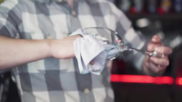 男性バーテンダーがバーに乾いたナプキンで濡れたガラスを拭いている背景 バーテンダーがカウンターの近くのガラスを磨く — ストック動画
