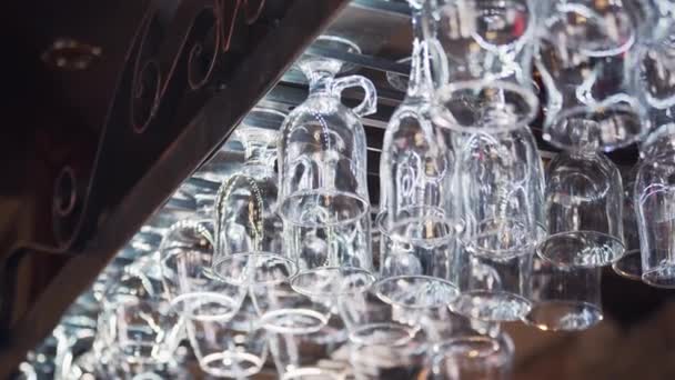 挂在酒吧柜台上方的玻璃器皿支架上的不同眼镜 在酒吧里倒置干净的眼镜 — 图库视频影像