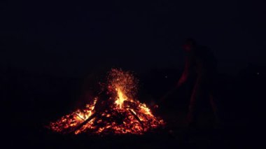 bir adam yangında kömürlerin yanma çatal düzeltiyor. karanlık gökyüzü karşı bir ateşten kıvılcım
