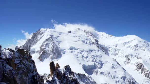 Picos rocosos cubiertos de nieve de las montañas alpinas. Montaña del Mont Blanc en una nube contra un cielo azul — Vídeo de stock