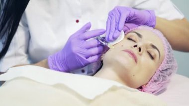 Beautician salonda iğne ile şırınga kullanarak genç kadın için yüzünde bir cilt dikmek yapar. Yüz enjeksiyon prosedürü