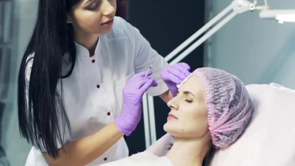 美しい医者はやわらかく女性の顔を刺す 額にヒアルロン酸注射を受けた若い女性の肖像 — ストック動画