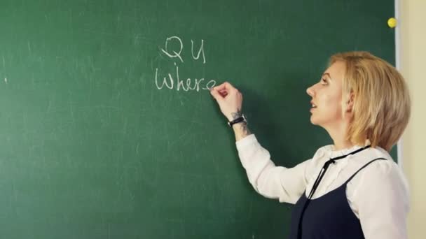 In an English class, a teacher writes with chalk on a blackboard and teaches students a lesson.