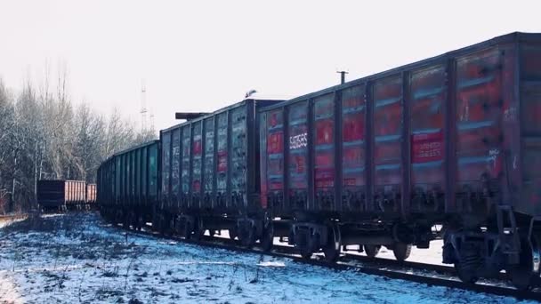 Een oude goederentrein met lading beweegt op rails op een heldere sneeuwdag — Stockvideo