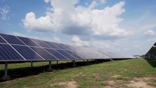 Rijen zonnepanelen op groen gras tegen een blauwe hemel met wolken. Zonne-energie station in het veld. — Stockvideo