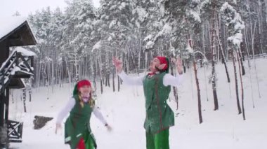 Kız ve erkek elfler beyaz karla oynarlar. Elfler Noel Baba 'nın ahşap evine kaçar..