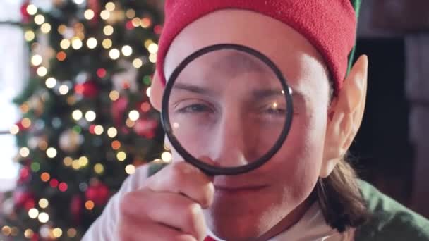 在靠近圣诞树的房间里 精灵男孩拿着放大镜玩耍 — 图库视频影像